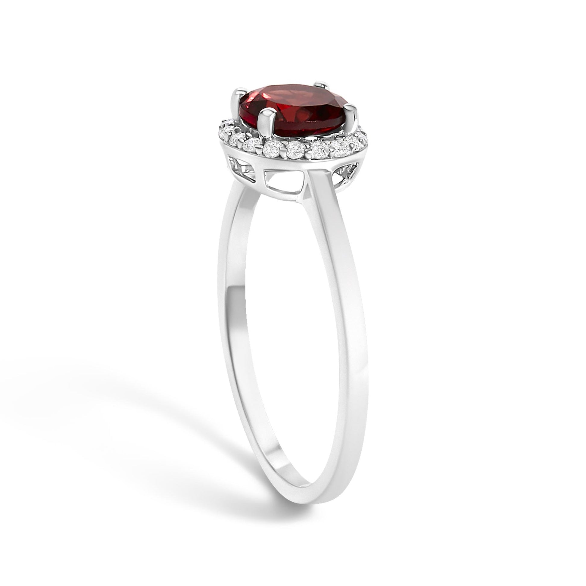 White metal ring with a round red gemstone held by four prongs, surrounded by a circle of small round white gemstones in shared prong setting, shown from a side angle.