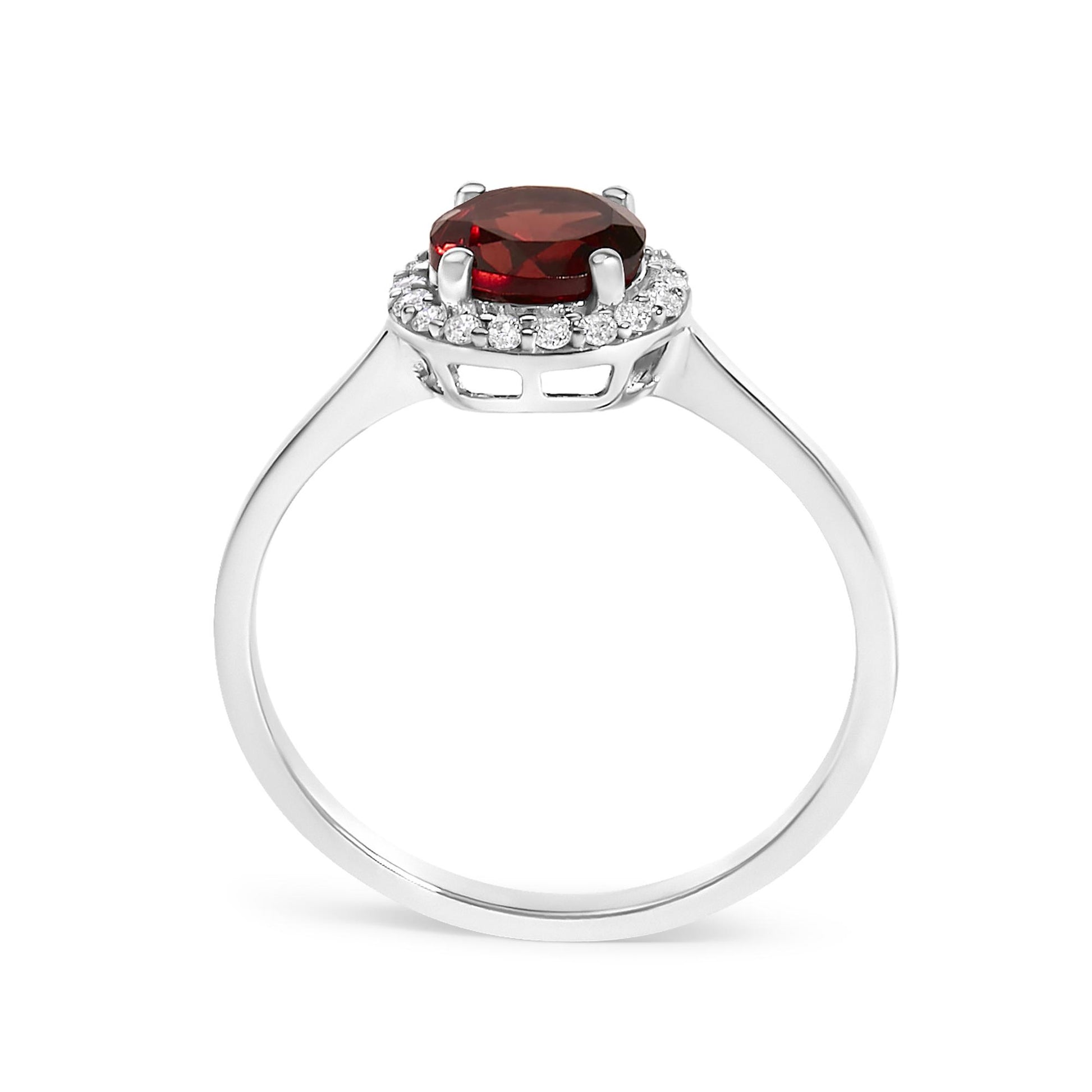 Close-up front view of a white metal ring featuring a round red gemstone set in four prongs surrounded by a halo of round white gemstones in shared prong setting.