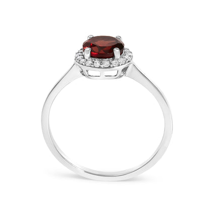 Close-up front view of a white metal ring featuring a round red gemstone set in four prongs surrounded by a halo of round white gemstones in shared prong setting.