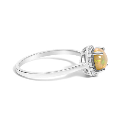 Side angle view of a white ring featuring a round multi-color opal gemstone set in a four-prong setting, surrounded by a halo of round white gemstones in shared prong settings.