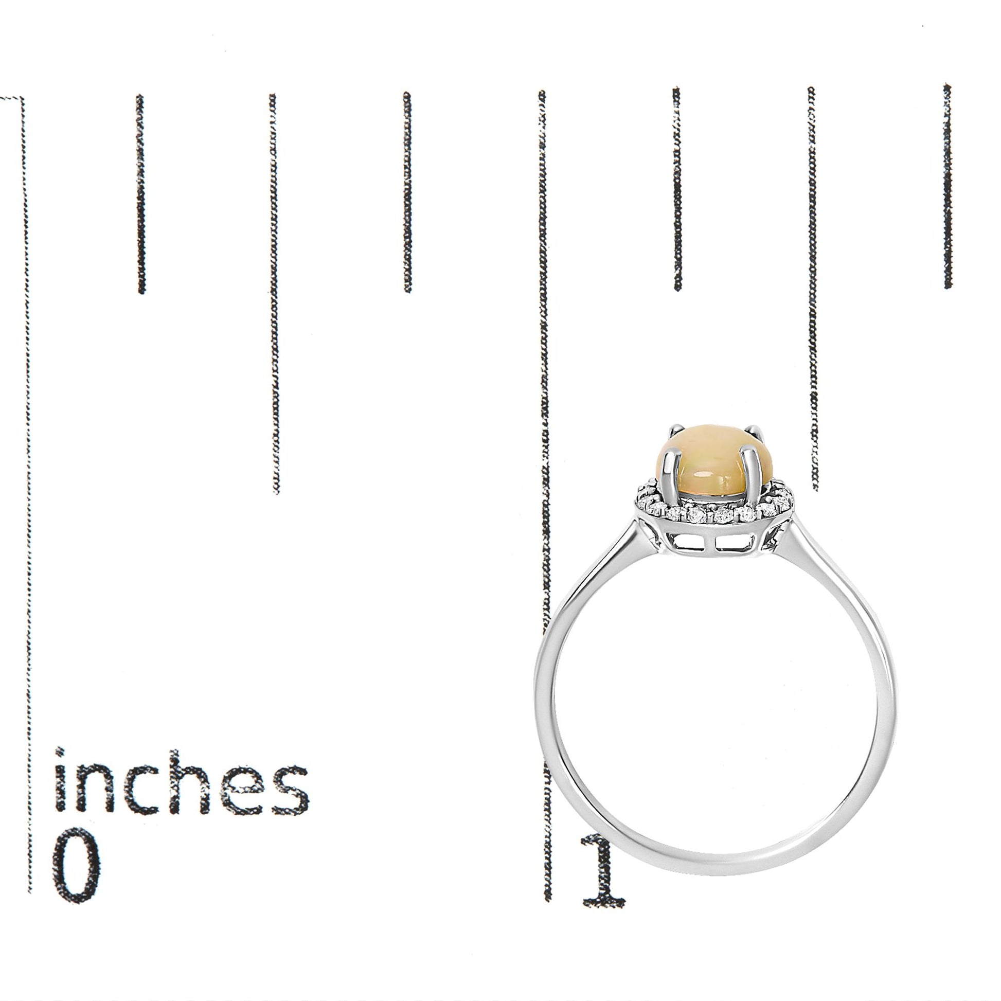 White metal ring with a round multi-color gemstone held by four prongs, surrounded by a halo of small round white gemstones in shared prong settings, shown from a side angle on a measurement scale.