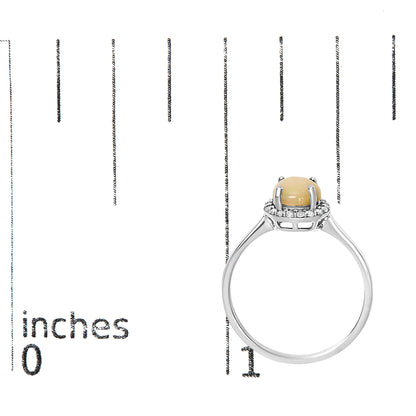 White metal ring with a round multi-color gemstone held by four prongs, surrounded by a halo of small round white gemstones in shared prong settings, shown from a side angle on a measurement scale.