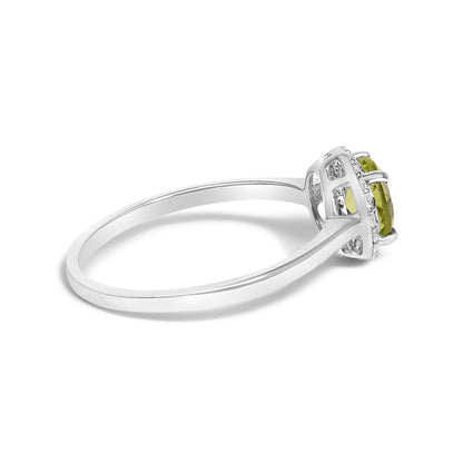 White metal ring with a round green gemstone set in a four-prong setting, surrounded by smaller round white gemstones in a shared prong setting, shown from the side angle.