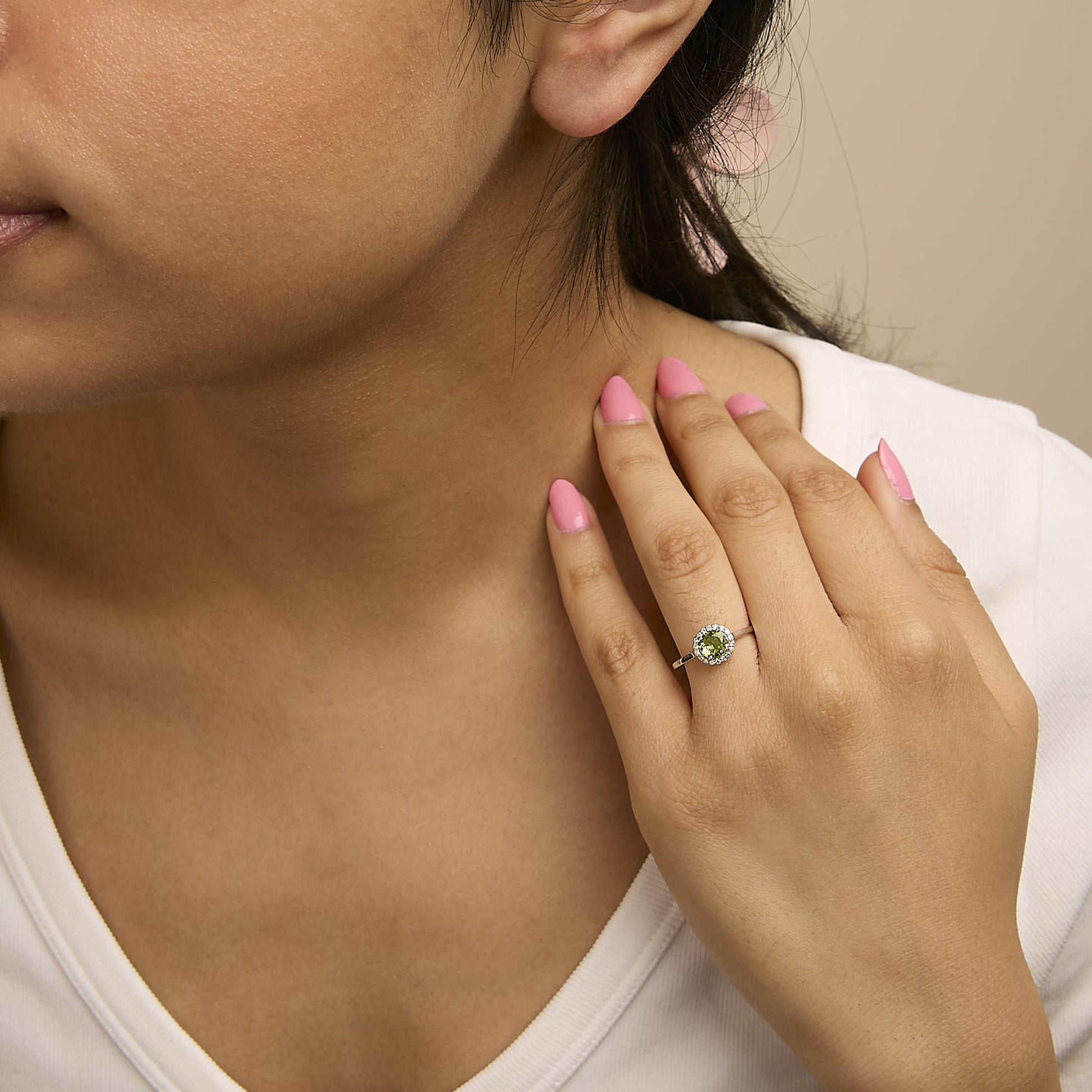 White metal ring with a round green gemstone center surrounded by round white gemstones in shared prong setting, shown worn on a model's hand from a side angle.