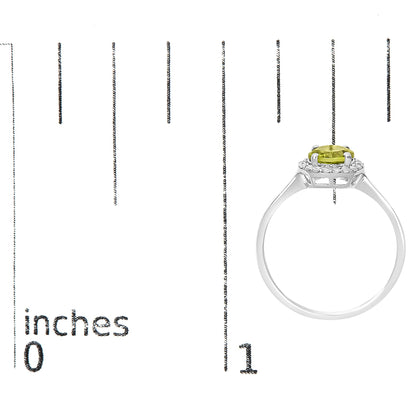 Ring shown on a scale, side view, featuring a white metal band with a round green gemstone held by four prongs at the center, surrounded by small round white gemstones in a shared prong setting.