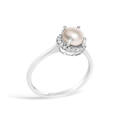 White metal ring with a round pearl center gemstone surrounded by a halo of small white round gemstones in a shared prong setting, shown in a close-up angled view.