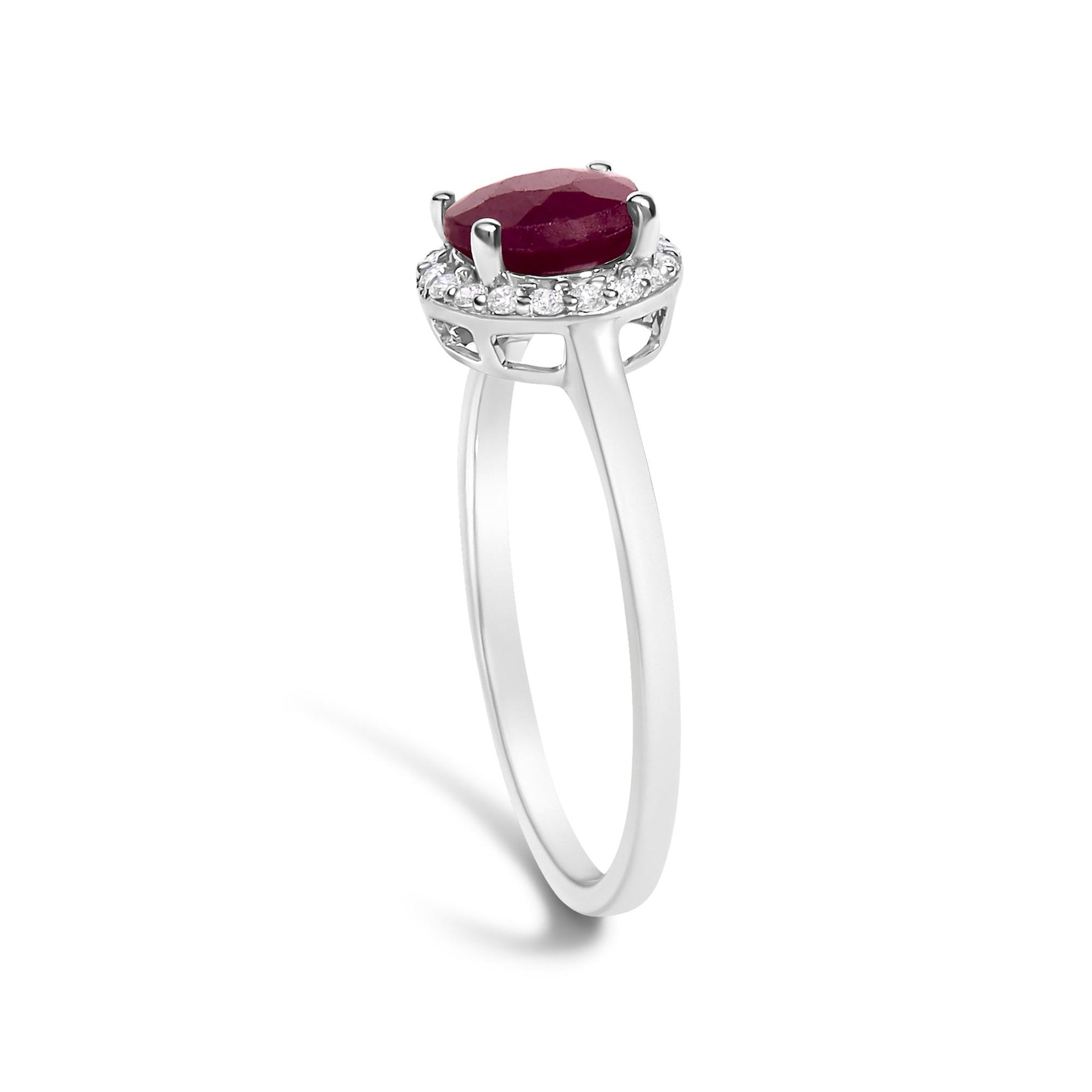 White metal ring shown from a side angle with a round red gemstone set in four prongs on top, surrounded by small round white gemstones in a shared prong setting.