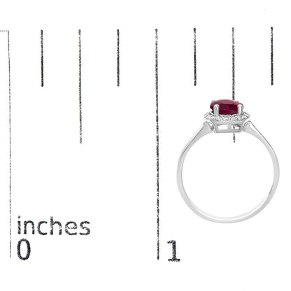 White metal ring with round red gemstone in a four-prong setting, surrounded by small white round gemstones, shown on a scale from a side angle.