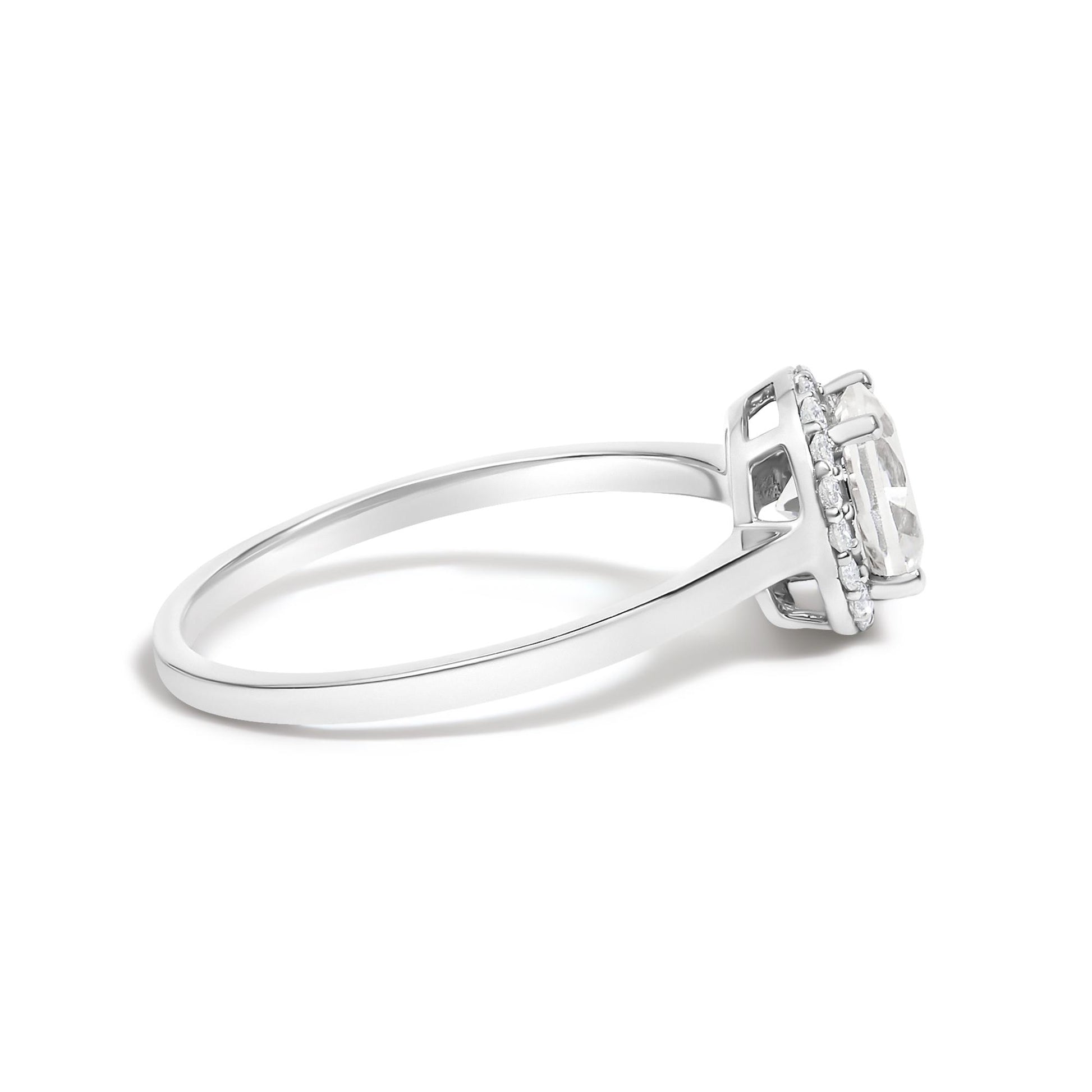 Side view of a white metal ring with a round center white gemstone in a four-prong setting, surrounded by a halo of smaller round white gemstones in shared prong settings. Ring shown against a white background.