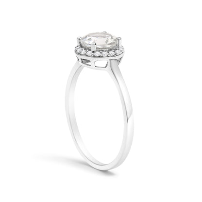 White metal ring with a raised round white gemstone held by four prongs, surrounded by a halo of smaller round white gemstones in shared prong settings, shown from a side angle on a white background.