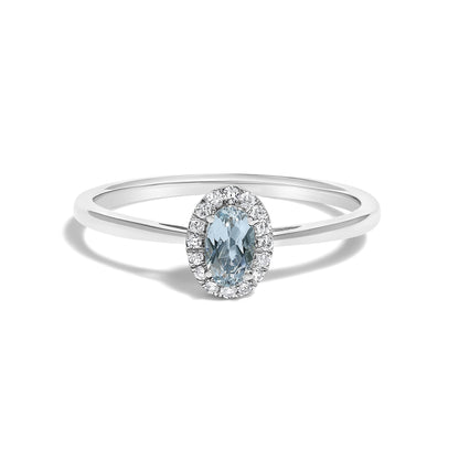 White metal ring with a blue oval gemstone center surrounded by small white round gemstones in a micro-pave setting, shown in a front-on angle.