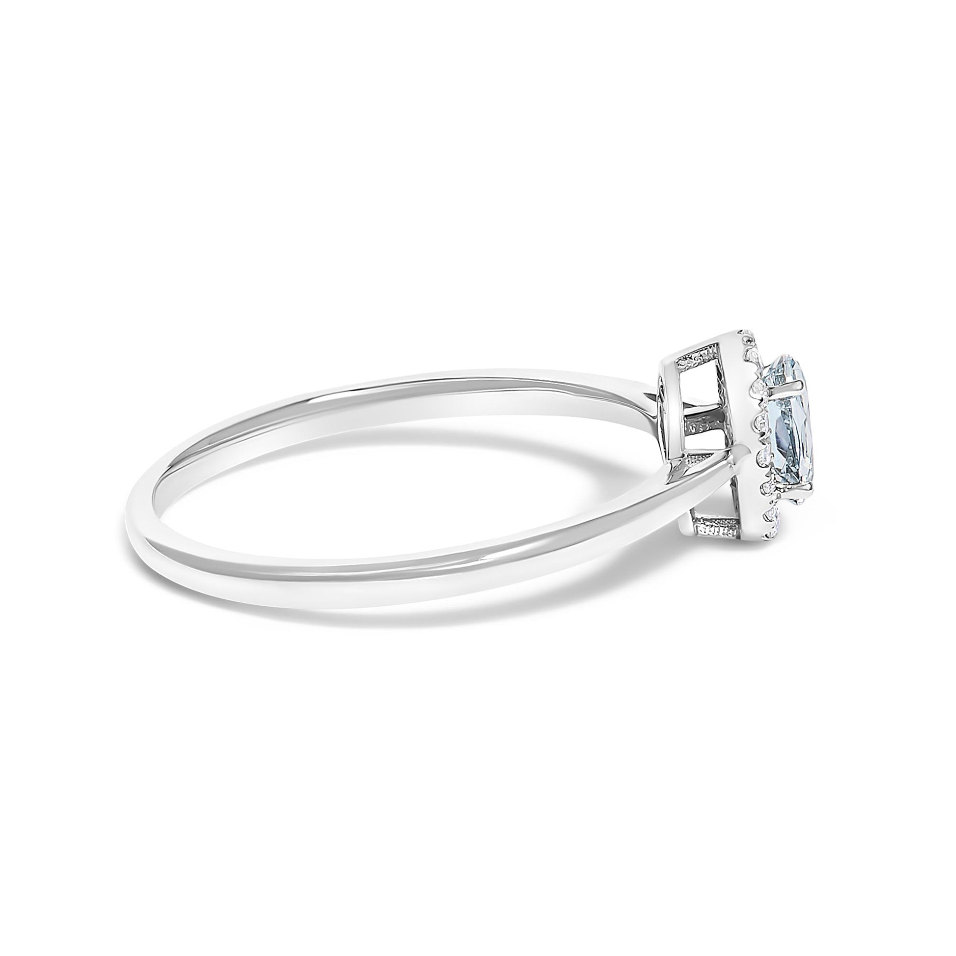 Side angle view of a white metal ring featuring an oval blue gemstone in a prong setting surrounded by a halo of small round white gemstones in a micro-pave setting.
