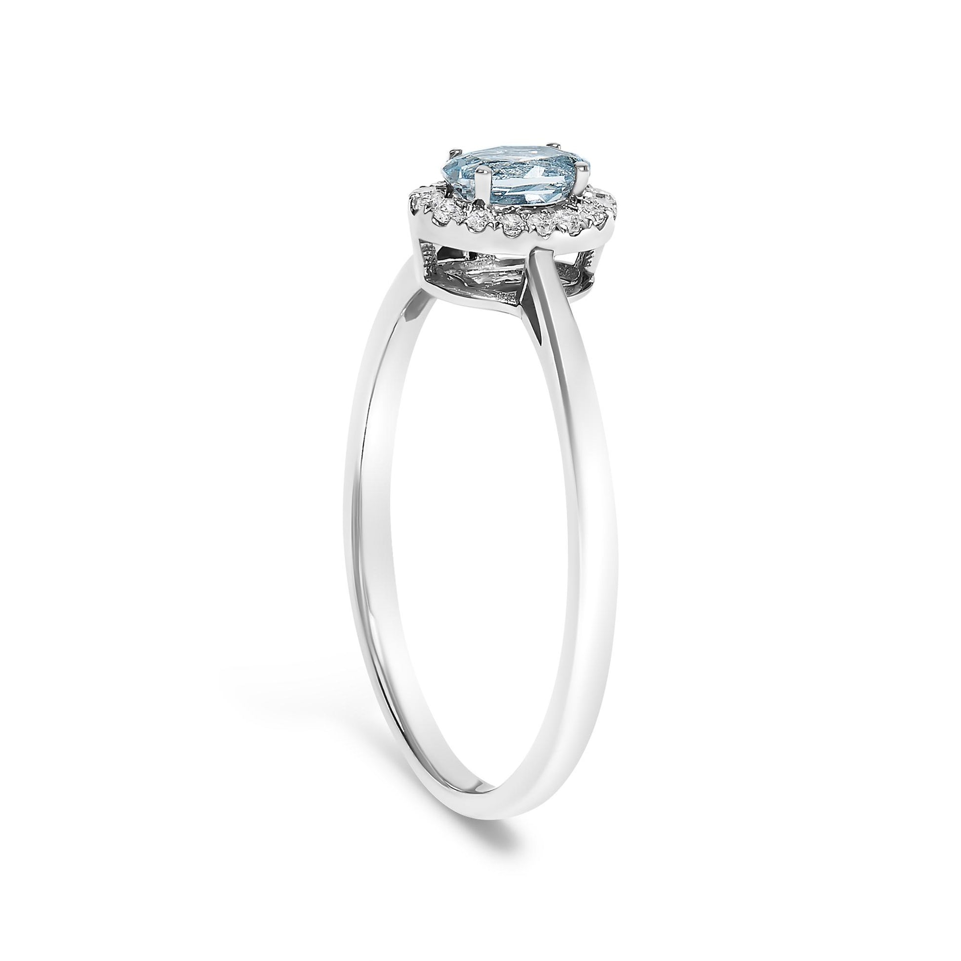 White metal ring with an oval blue gemstone in a prong setting surrounded by round white gemstones in a micro-pave setting, shown in a side angle.