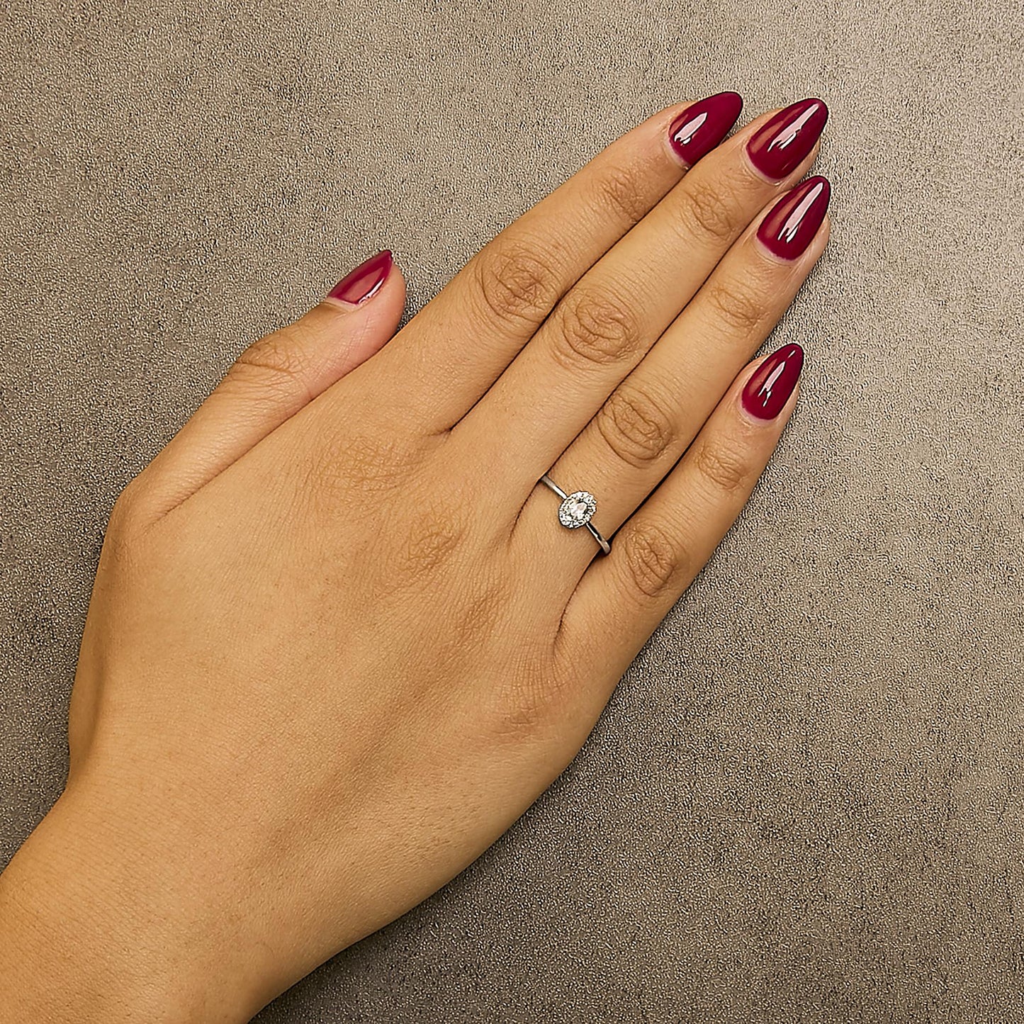 White metal ring with an oval blue gemstone surrounded by round white gemstones in a micro-pave setting, shown worn on a model's hand from a top-down angle.