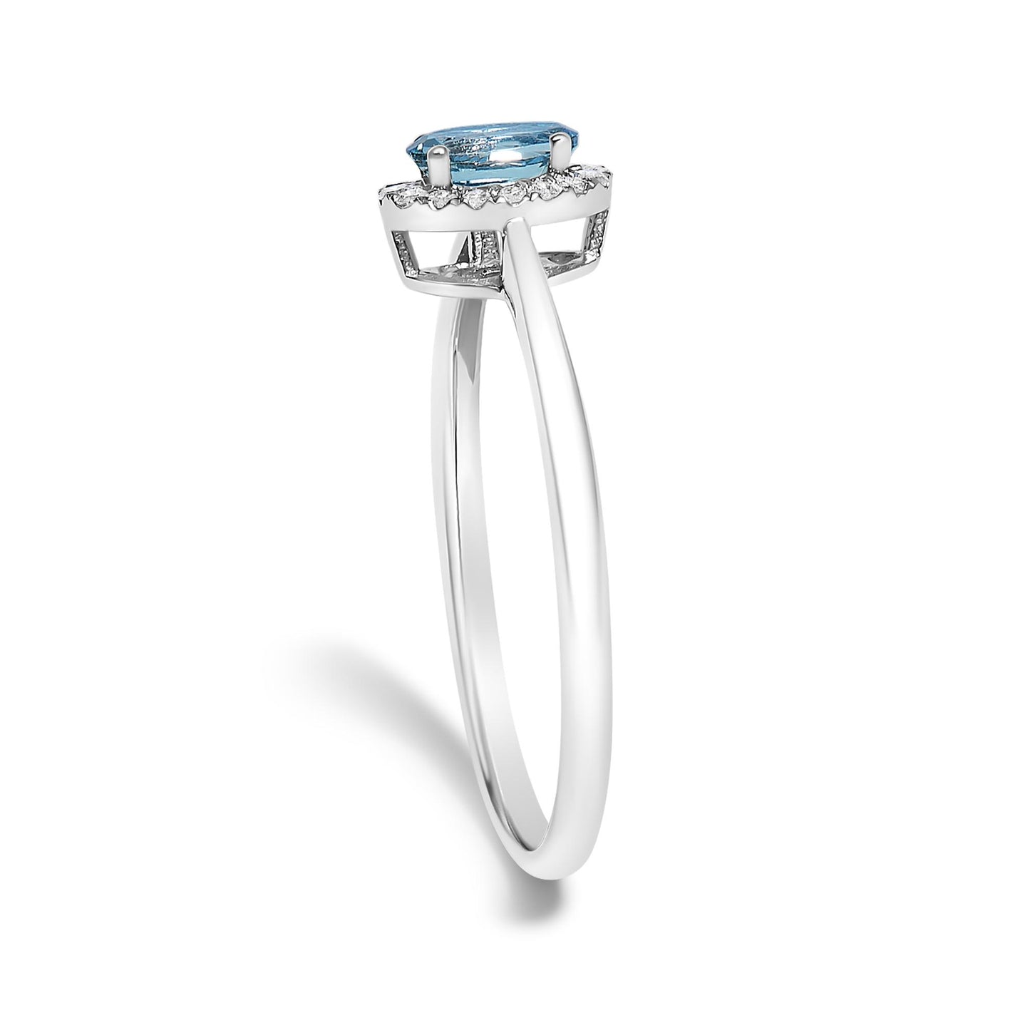 White metal ring with an oval blue gemstone set in prongs, surrounded by a halo of small white gemstones in micro-pave setting, shown from a side angle on a white background.