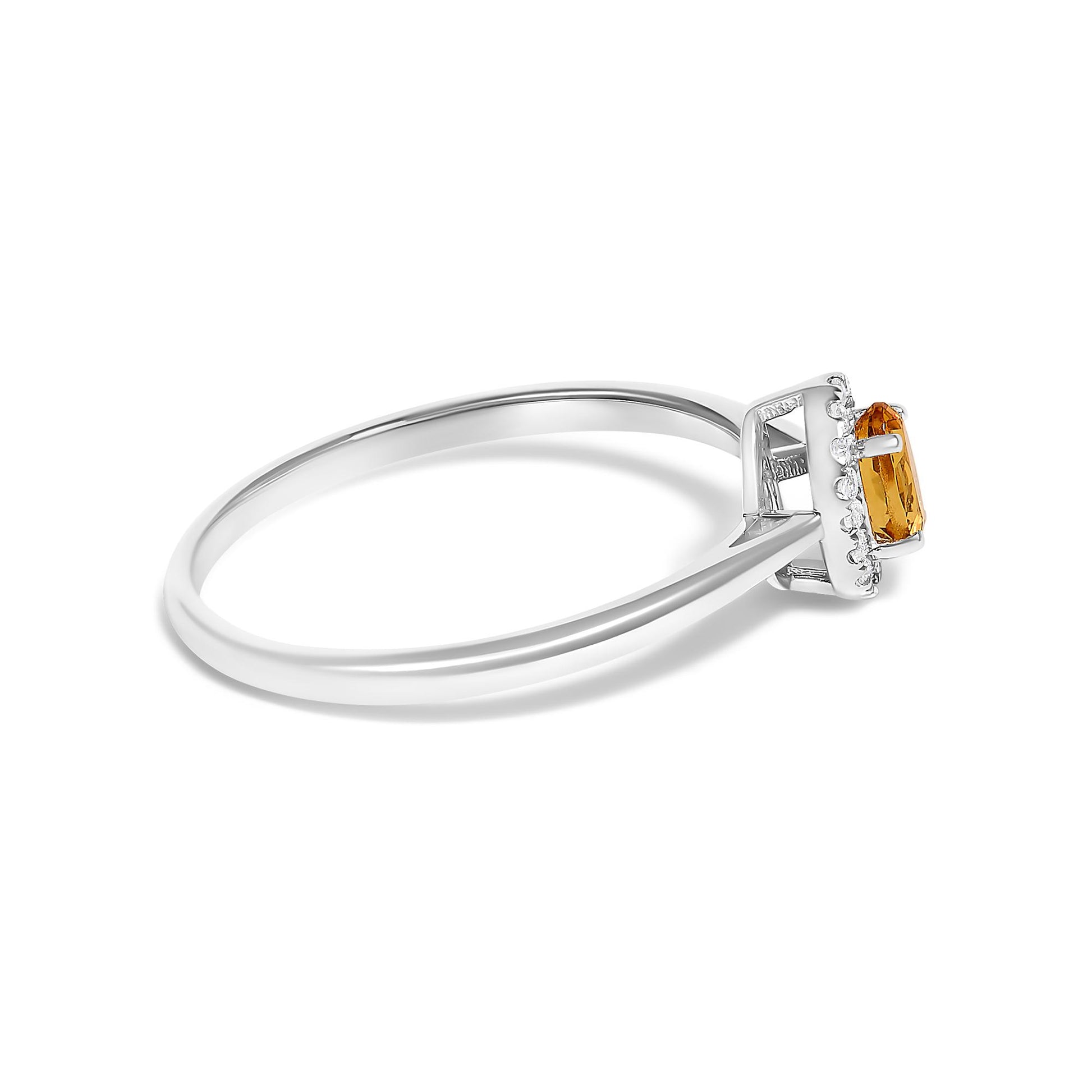 Side view of a white metal ring with an oval orange gemstone in a prong setting, surrounded by small round white gemstones in a micro-pave setting.