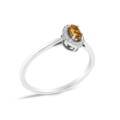 White metal ring shown at an angle with an oval orange gemstone set in the center surrounded by a halo of small white gemstones in a micro-pave setting.