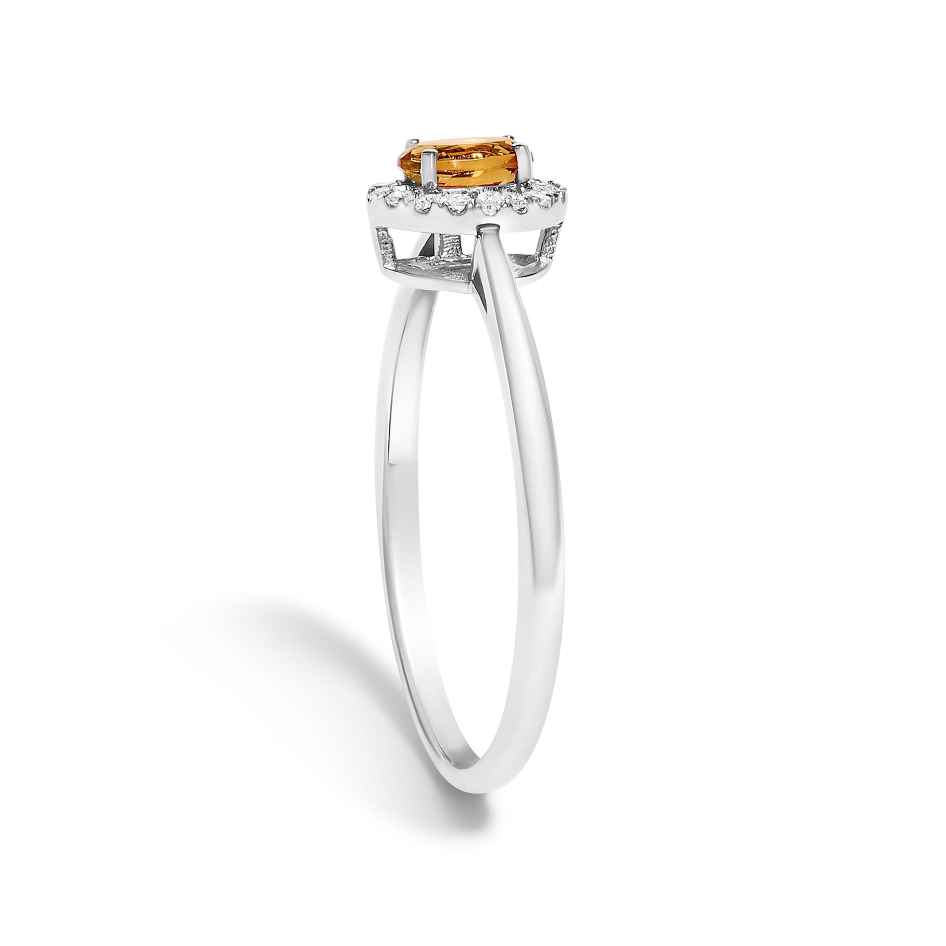 White metal ring with an oval orange gemstone in prong setting, surrounded by a halo of small round white gemstones in micro-pave setting, shown in a side angle on a white background.