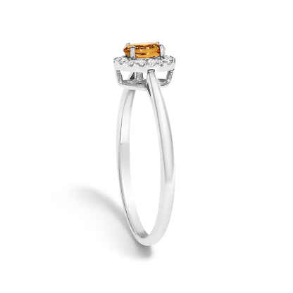 White metal ring with an oval orange gemstone in prong setting, surrounded by a halo of small round white gemstones in micro-pave setting, shown in a side angle on a white background.