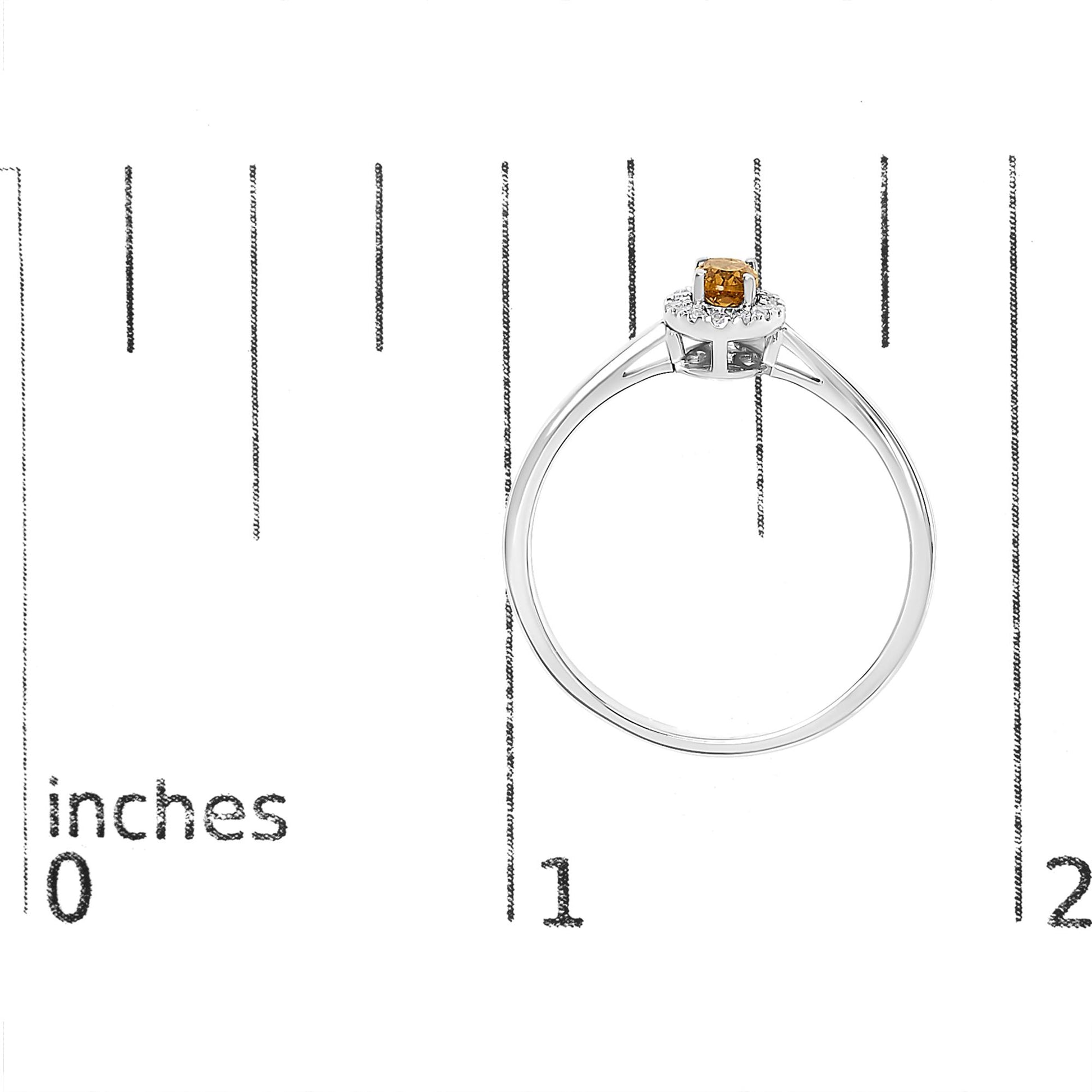 White metal ring with single oval orange gemstone in prong setting, surrounded by small round white gemstones in a circular micro-pave setting, shown on a scale from a side angle.