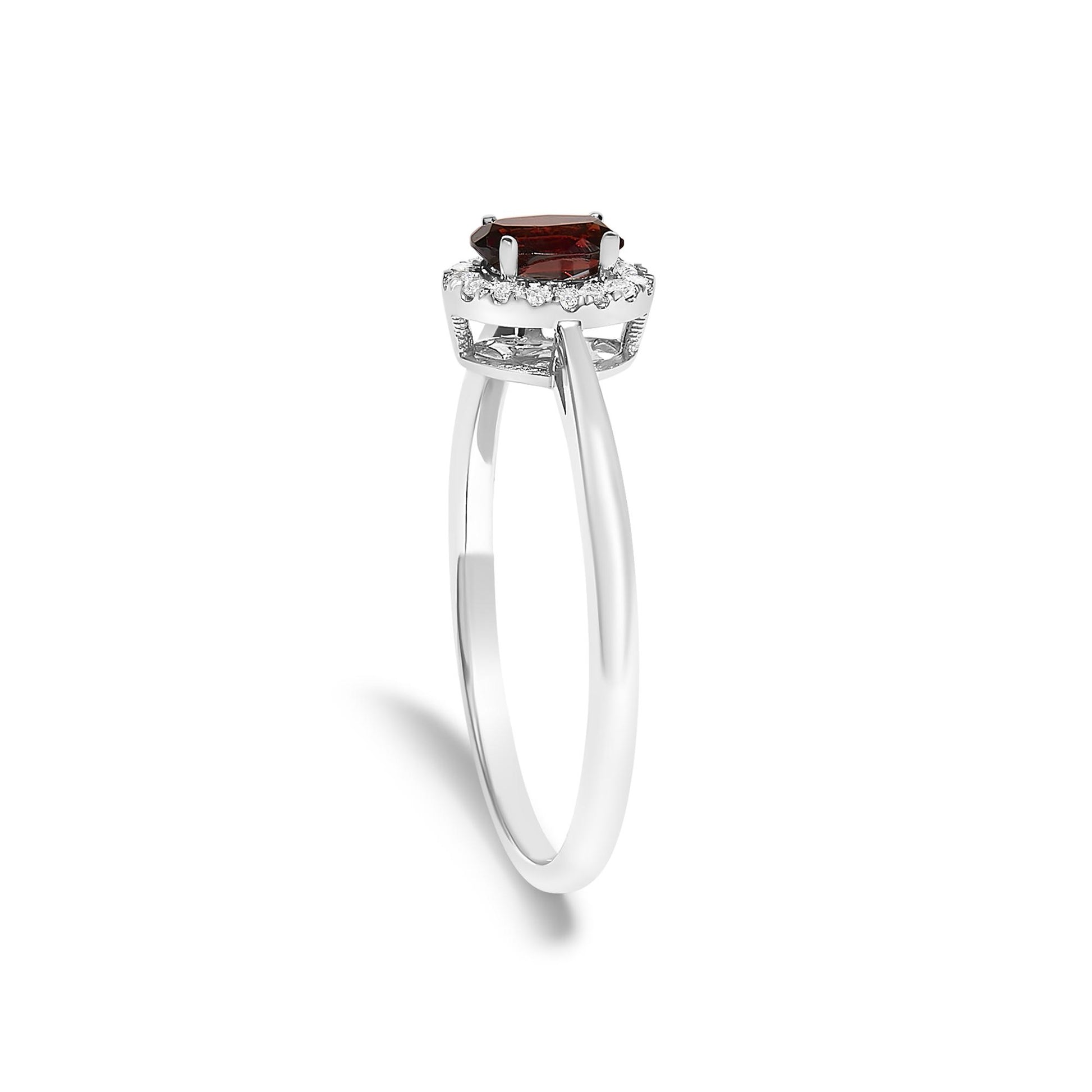 White metal ring shown at a slight side angle with an oval red gemstone in a prong setting surrounded by small round white gemstones in a micro-pave setting.