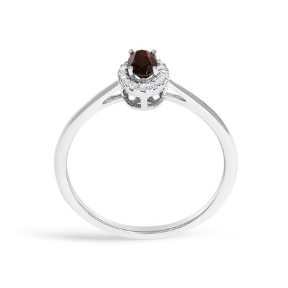 White metal ring shown from the top angle with an oval red gemstone in prong setting surrounded by round white gemstones in a micro-pave setting.