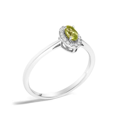 White metal ring with an oval green gemstone set in prongs, surrounded by small white gemstones in a micro-pave setting, shown at a slight angle on a white background.