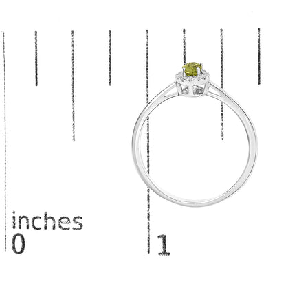 White metal ring with a round setting featuring one oval green gemstone in the center, surrounded by small white gemstones in a micro-pave setting, shown on a scale from a side angle.