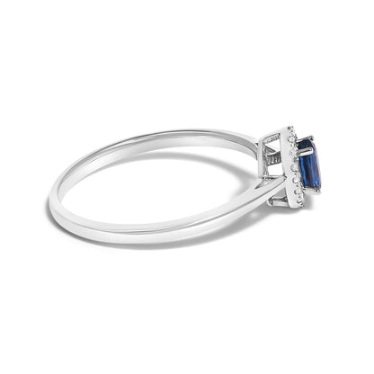 Side angle close-up of a white metal ring with a blue oval gemstone set in prongs, surrounded by small white round gemstones in a micro-pave setting.