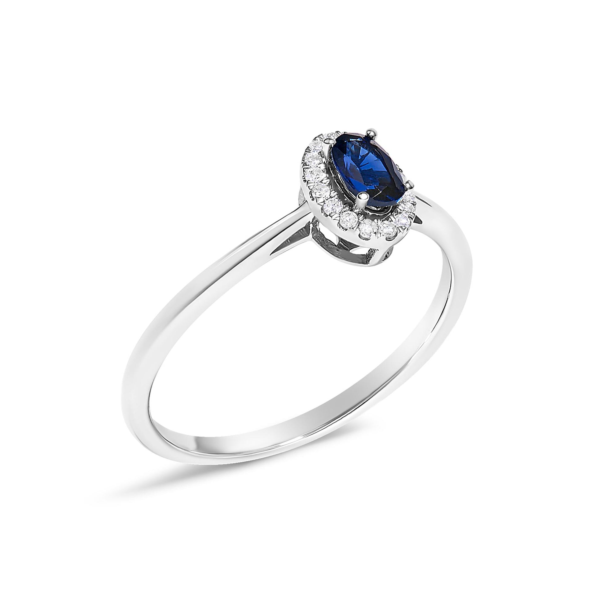 White metal ring with an oval blue gemstone in a prong setting, surrounded by a halo of small round white gemstones in a micro-pave setting, shown at a slight angle on a white background.