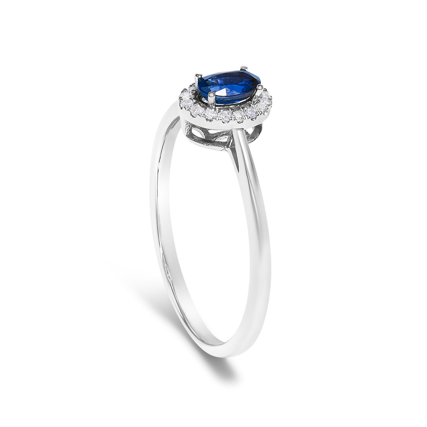White metal ring shown from a slightly angled side view, featuring an oval blue gemstone in a prong setting surrounded by a halo of small round white gemstones in a micro-pave setting.