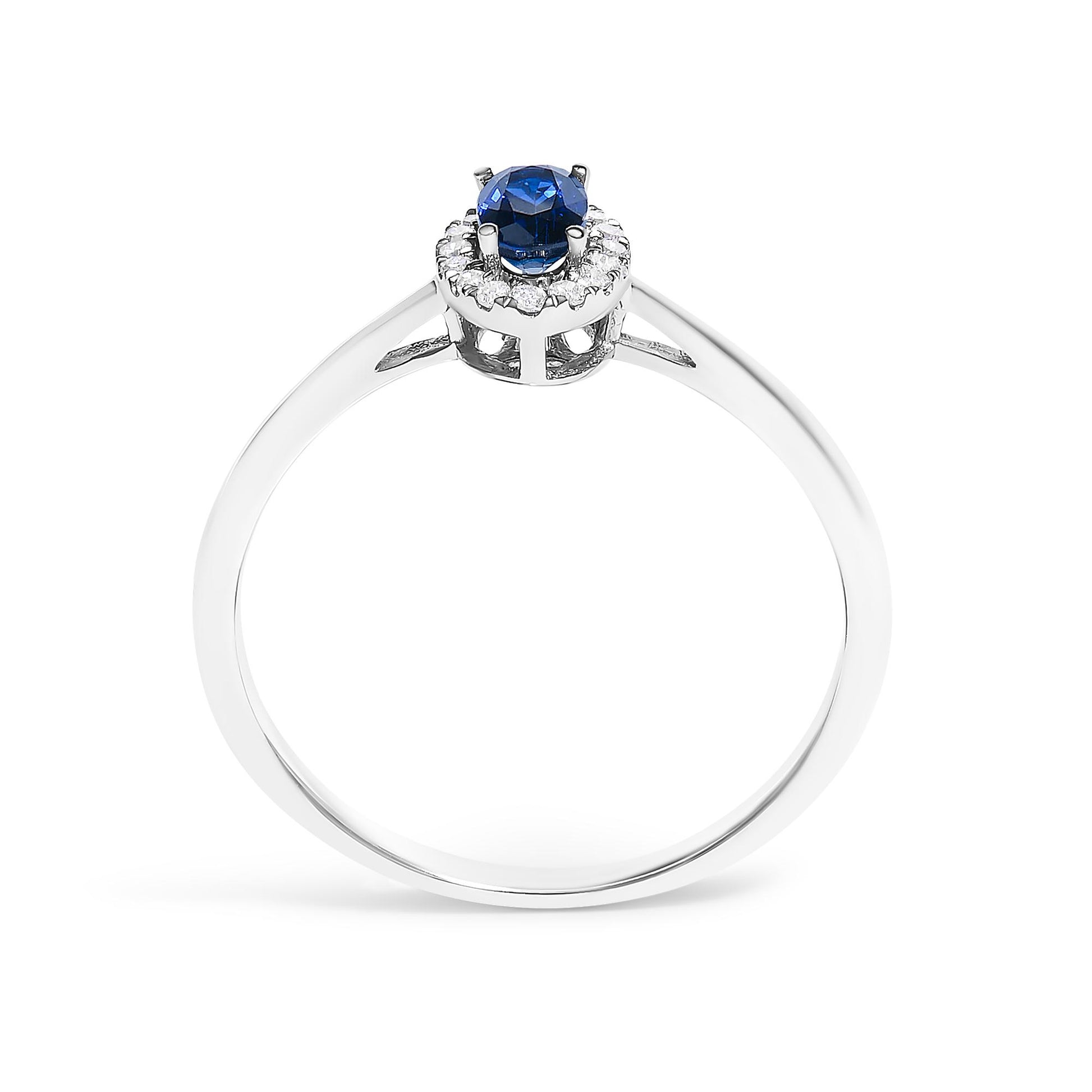 White metal ring shown from the front angle, featuring a central oval blue gemstone in a prong setting surrounded by a halo of small round white gemstones in micro-pave setting.
