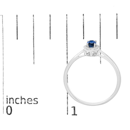 White metal ring with an oval blue gemstone in a prong setting surrounded by small round white gemstones in a micro-pave setting, shown on a scale from a side angle.