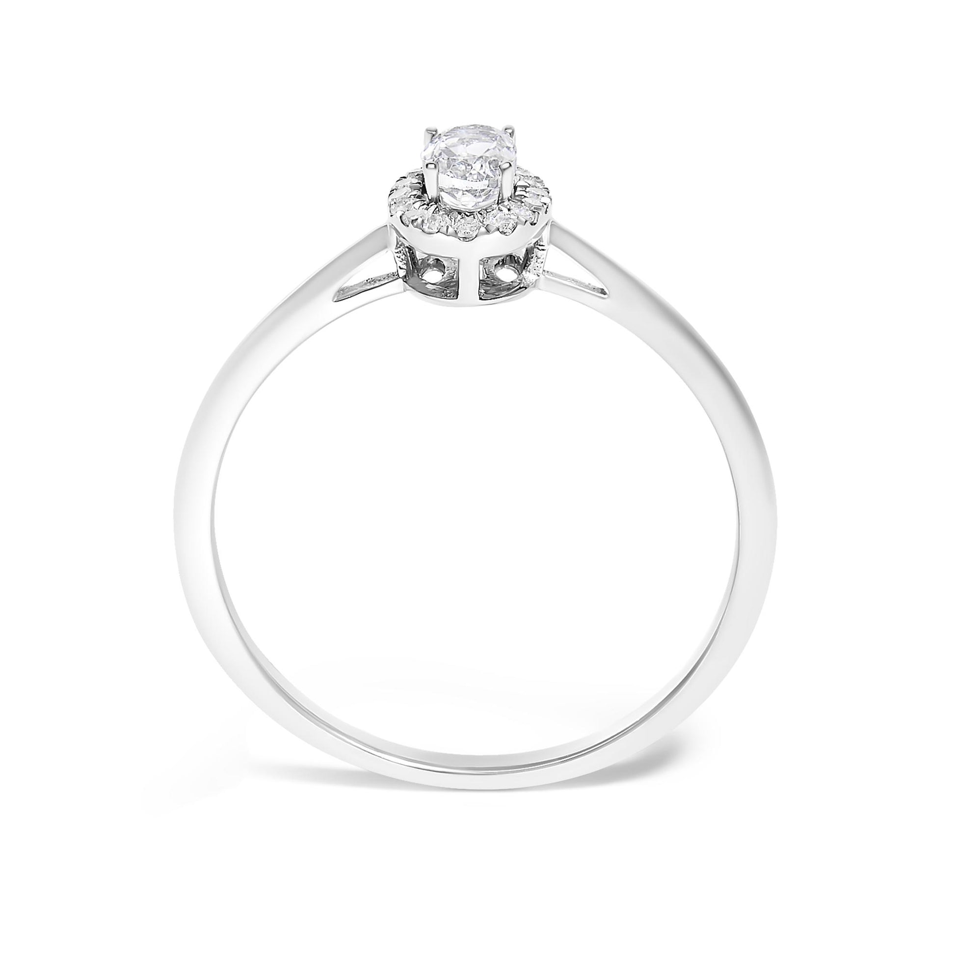 Close-up side view of a white metal ring featuring a single oval white gemstone set in prongs, surrounded by a halo of small round white gemstones in micro-pave setting.