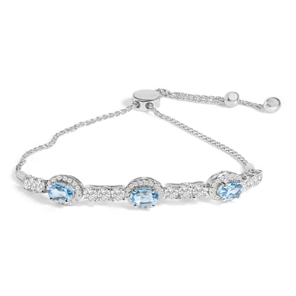 White metal bracelet with three oval blue gemstones surrounded by small white gemstones and additional white gemstones along the chain, shown in a close-up angled shot on a white background.