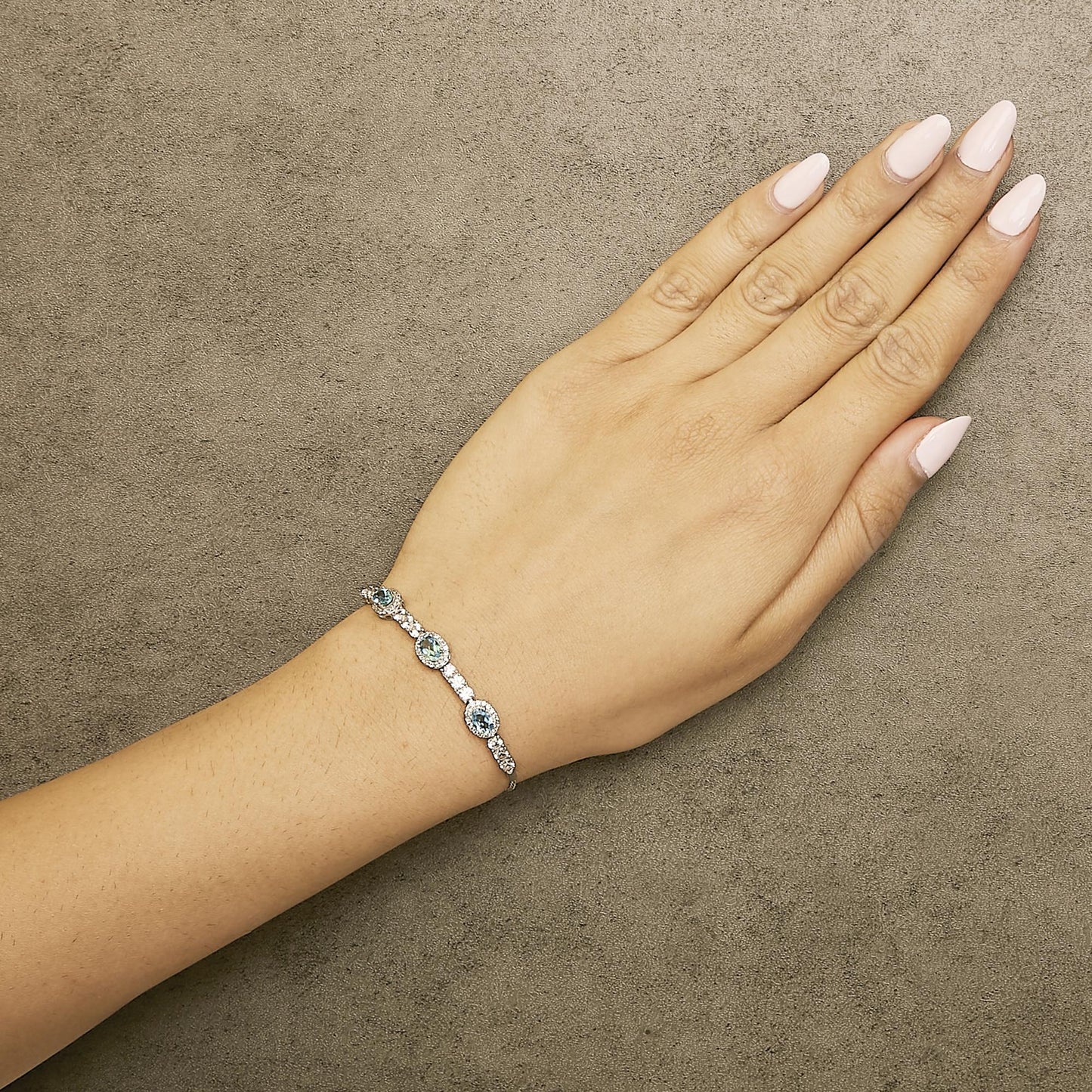 White bracelet with three oval blue gemstones surrounded by small white round gemstones in prong settings, shown worn on a model's wrist, angled top-down.