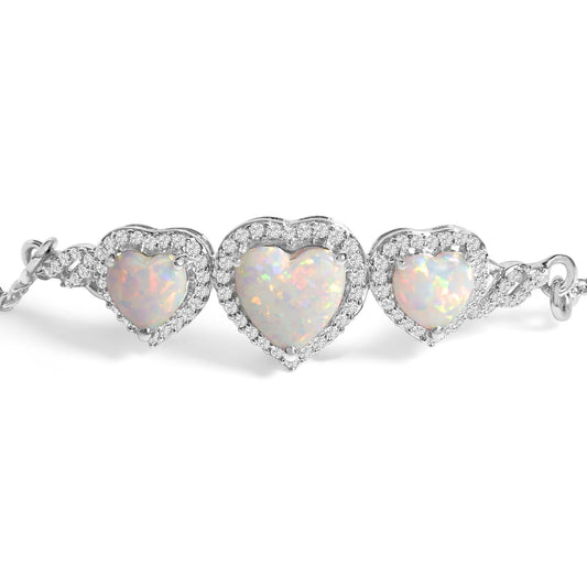 Close-up front view of a white metal bracelet featuring three heart-shaped white opal gemstones each surrounded by small round white gemstones in prong setting.