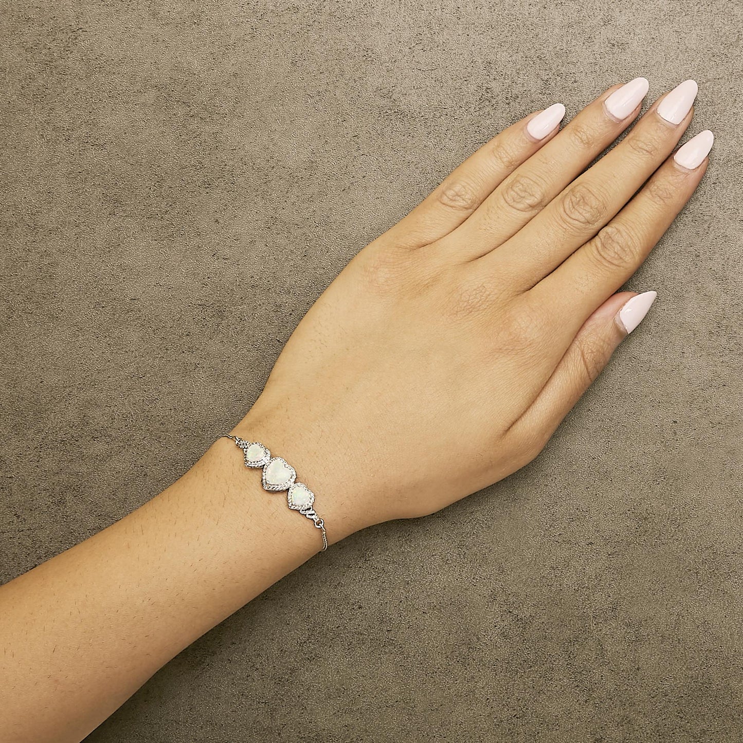 Bracelet with three white heart-shaped gemstones in prong setting on a white metal chain, shown worn on a model's wrist, top-down angle.