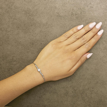 Bracelet with yellow and white metal featuring one white round gemstone in a four-prong setting and multiple smaller white round gemstones in prong settings, shown worn on a model's wrist from a top angle.