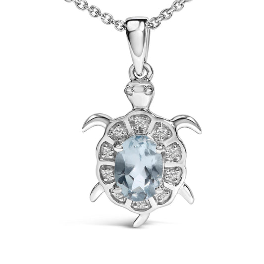 White metal necklace pendant in the shape of a turtle, featuring an oval blue gemstone in a four-prong setting at the center surrounded by smaller round white gemstones in prong settings, shown in a front close-up view.
