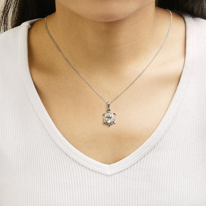 Necklace with a turtle-shaped pendant featuring an oval blue gemstone center surrounded by round white gemstones, shown worn on a model from the front.