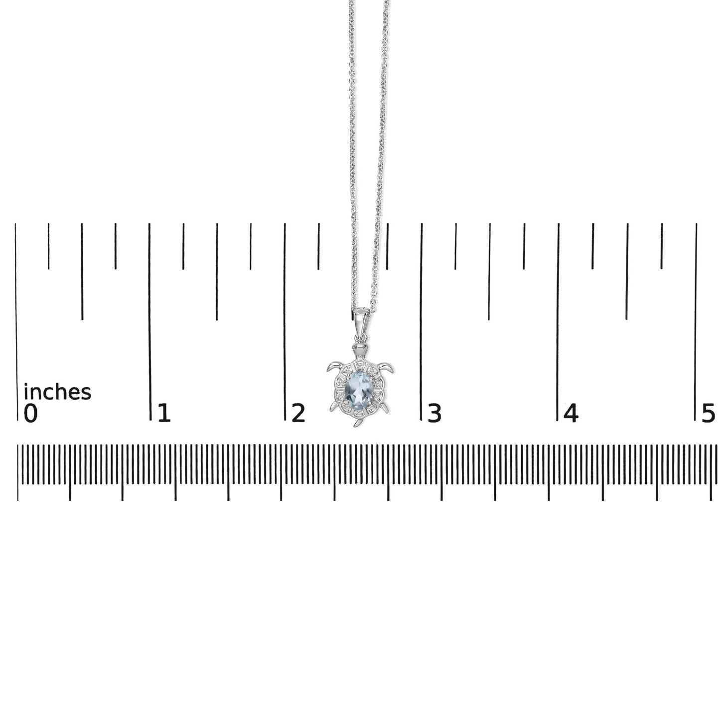 White metal turtle-shaped necklace with a central oval blue gemstone surrounded by small round white gemstones in prong settings, shown on a scale from a front angle.