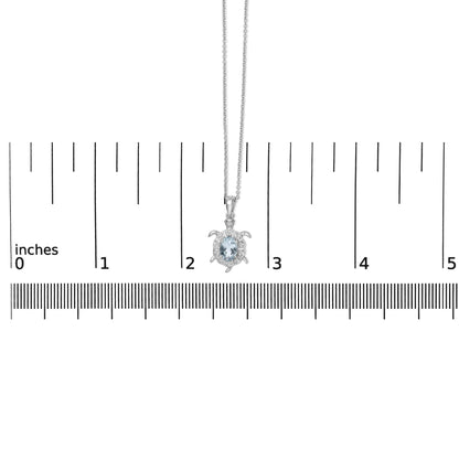 White metal turtle-shaped necklace with a central oval blue gemstone surrounded by small round white gemstones in prong settings, shown on a scale from a front angle.