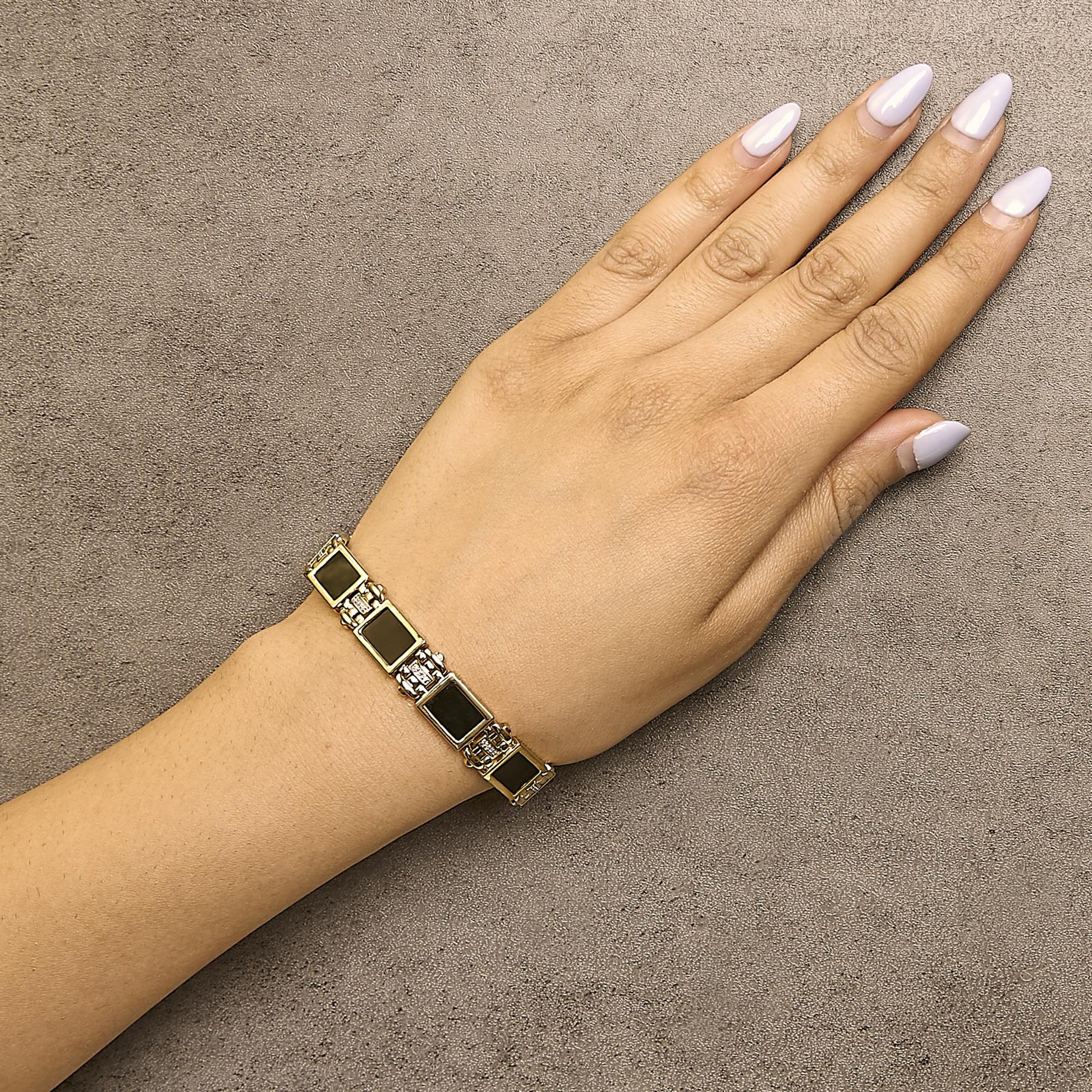 Yellow metal bracelet with rectangular black gemstones and small white gemstones in between, shown worn on a model's wrist from a top-down angle.