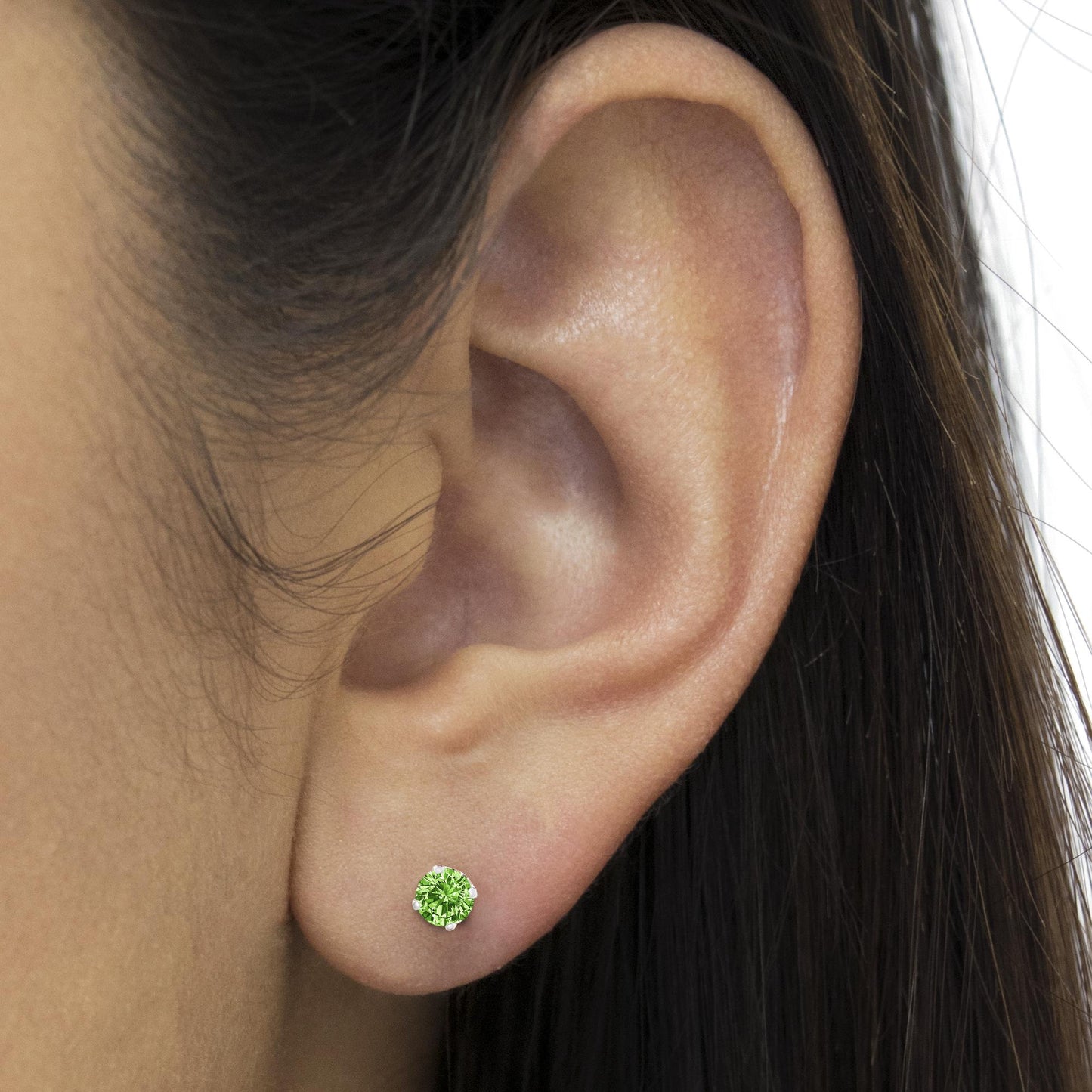 Close-up side view of a white metal stud earring with a round green gemstone in prong setting, worn on a model's ear.
