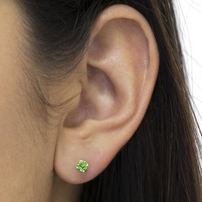 Close-up side view of a white metal stud earring with a round green gemstone in prong setting, worn on a model's ear.