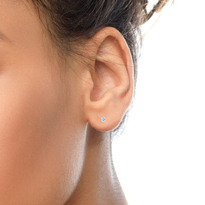 Close-up side view of a model wearing a single white metal stud earring with a round white gemstone in a 4-prong setting.