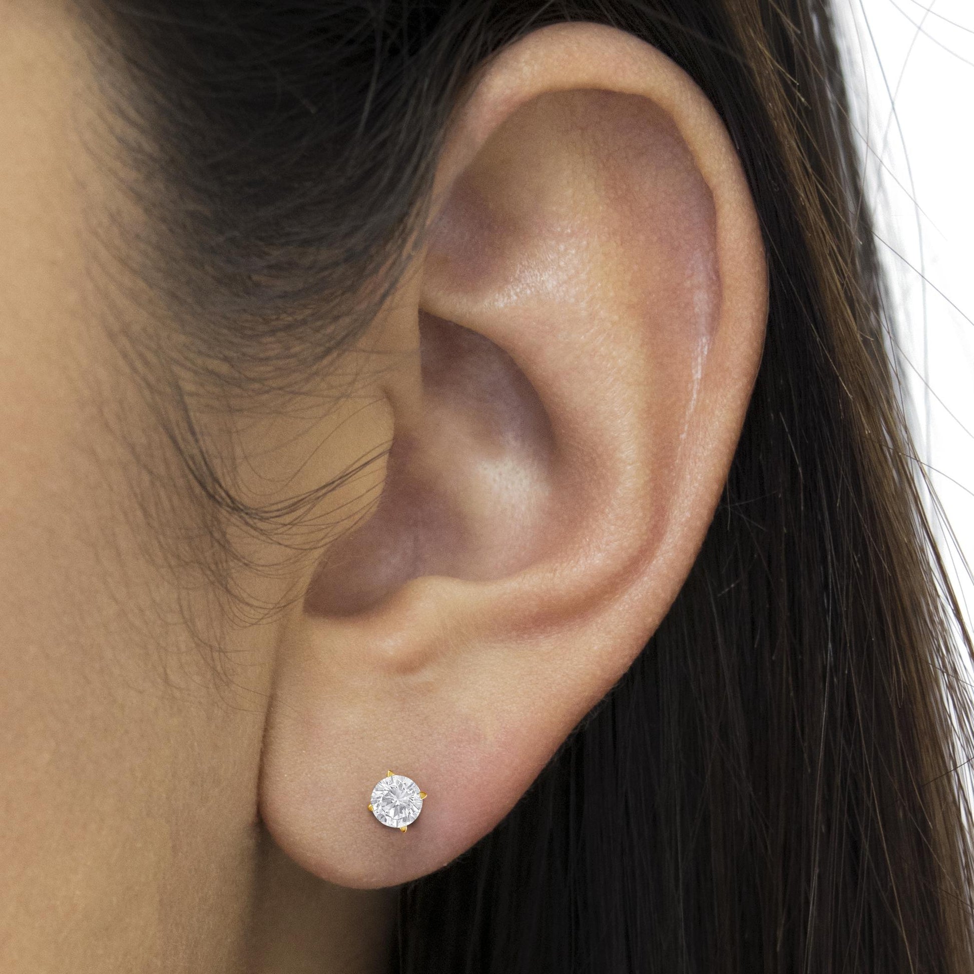 Close-up side view of a yellow metal stud earring with a round white gemstone in a prong setting, worn on a model's ear.