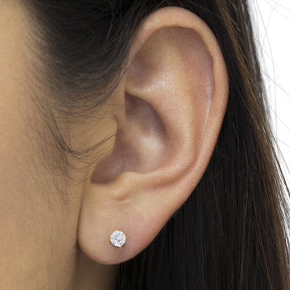 Close-up side view of a yellow metal stud earring with a round white gemstone in a prong setting, worn on a model's ear.