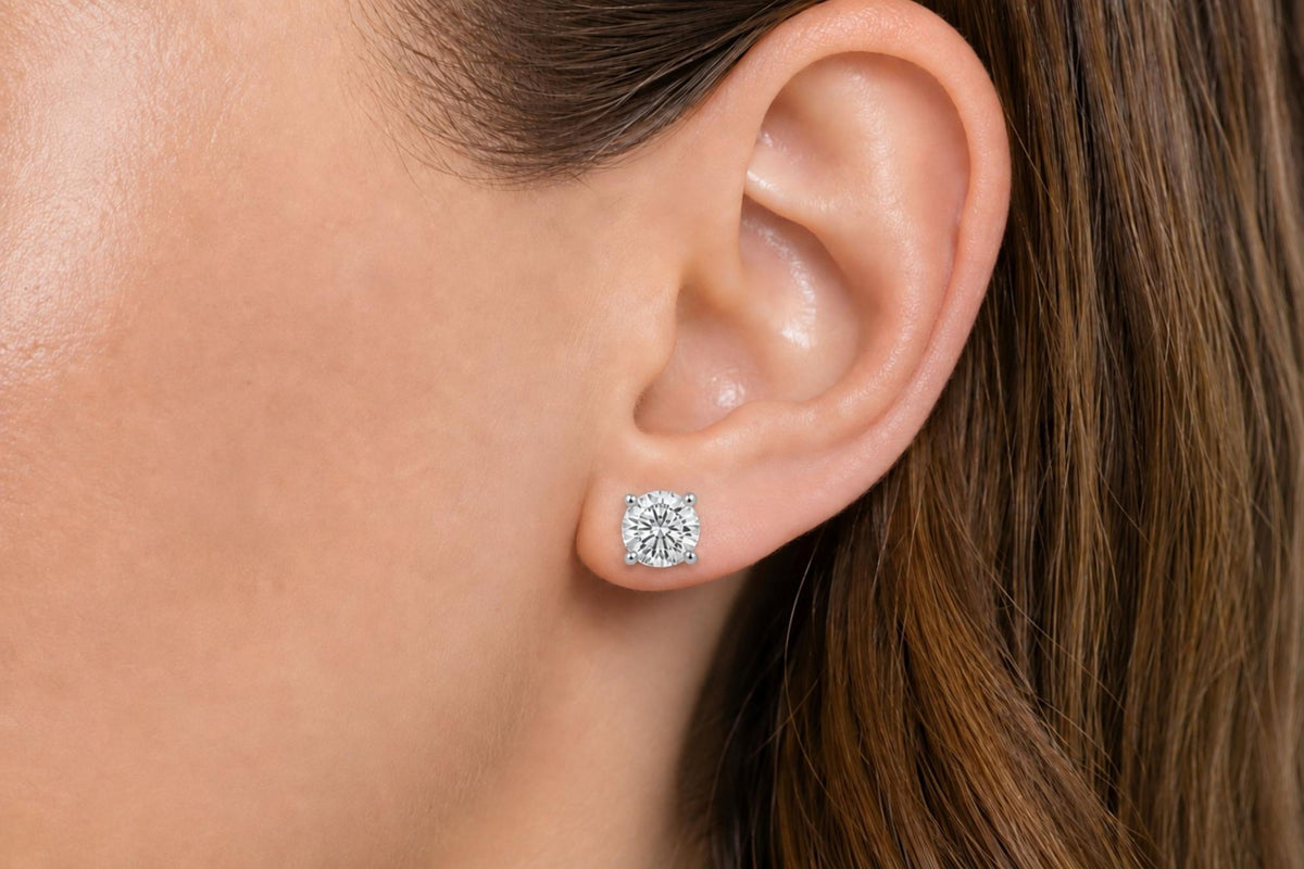 Close-up side view of a model wearing a white metal stud earring with a round white gemstone in a four-prong setting.